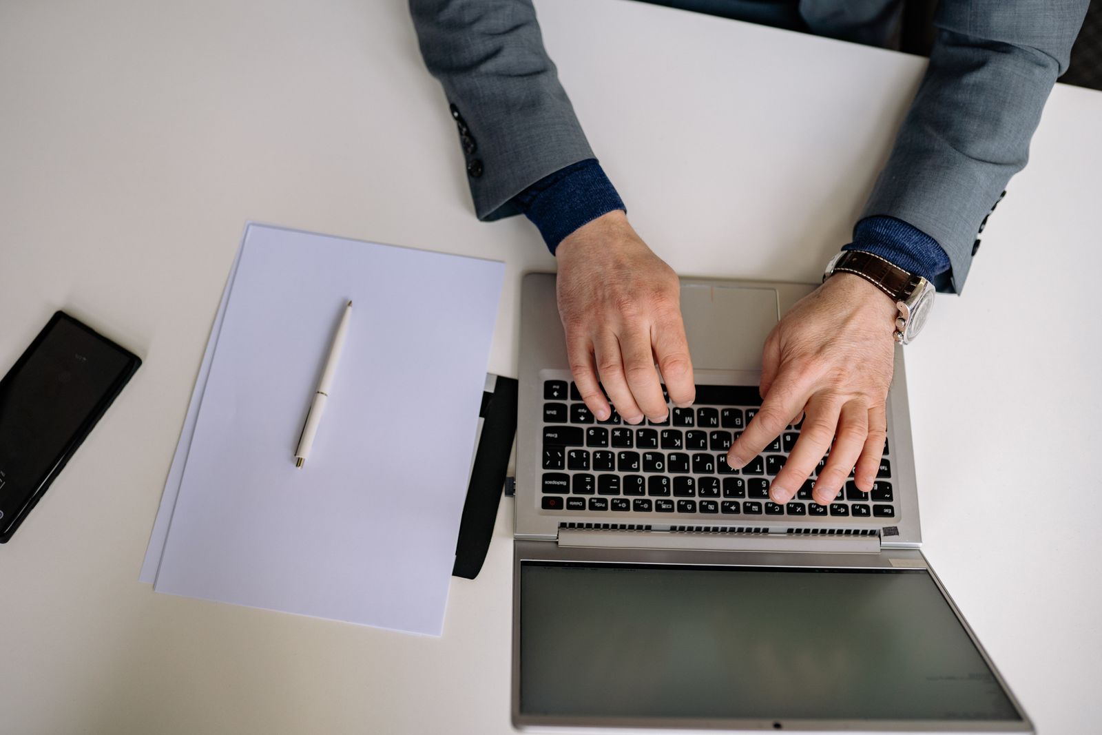 Overhead view of a financial advisor in a suit typing on a laptop beside a notepad and phone