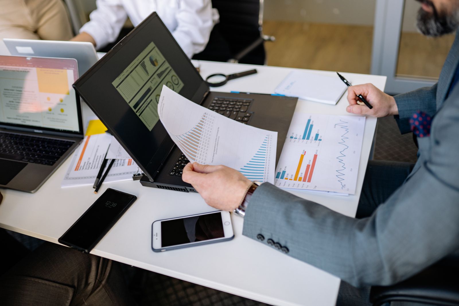 Advisor reviewing printed growth charts and performance reports next to two laptops in a meeting